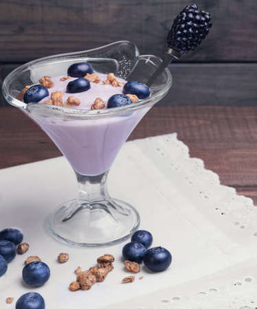 On a wooden background vintage rustic glass vases decorated with berries and granola yogurt, white cloth with embossed laceの写真素材