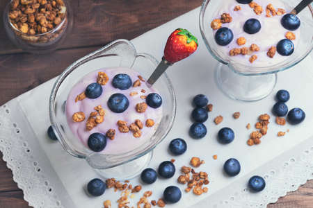 On a wooden background vintage rustic two glass vases decorated with berries and granola yogurt, white cloth with embossed laceの写真素材