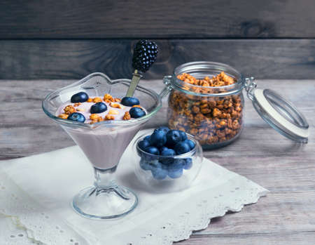 On a wooden background vintage rustic glass vases decorated with berries and granola yogurt, white cloth with embossed lace, glass jarの写真素材