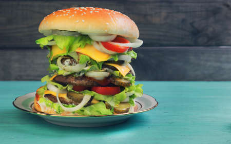 Big cheeseburger deluxe high on green wooden background in rustic style for gluttonsの写真素材
