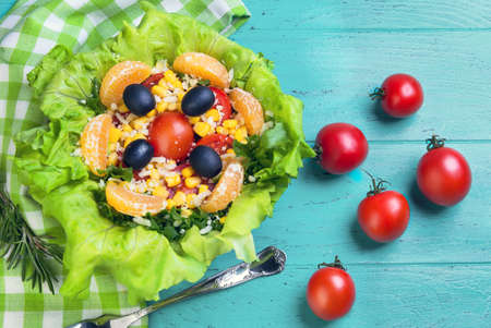 Salad green leaf lettuce, corn kernels, mandarin slices, grated cheese, cherry tomatoes, a sprig of rosemary, cloth napkins, black olives on a wooden light background, top viewの写真素材