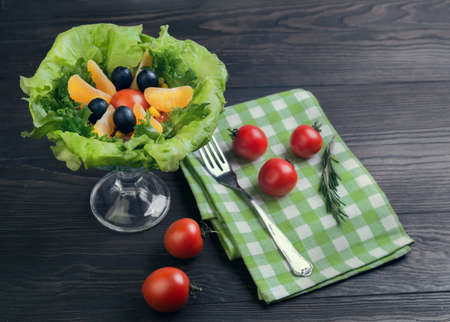 Salad green leaf lettuce, corn kernels, mandarin slices, grated cheese, cherry tomatoes, a sprig of rosemary, cloth napkins, black olives on a wooden light background, top viewの写真素材