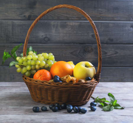 Wicker straw basket with an assortment of fruits and lemon, orange, grape, strawberry, berries Physalis, tangerine on a wooden table in a rustic styleの写真素材