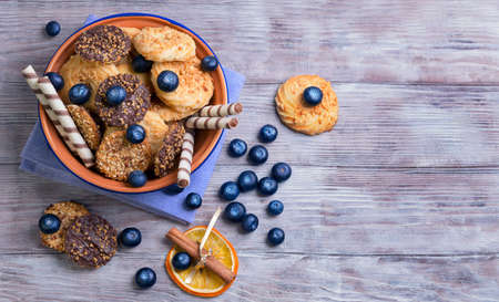 On a light wooden background blue ceramic bowl with cookies, decorated with a dried orange circle with a stick of cinnamon, blueberry, chocolate rolls, clothの写真素材
