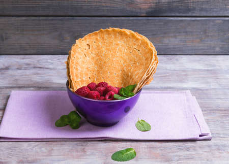 Delicate pancakes with holes in a purple mask on a light wooden table, mint leaves and raspberriesの写真素材
