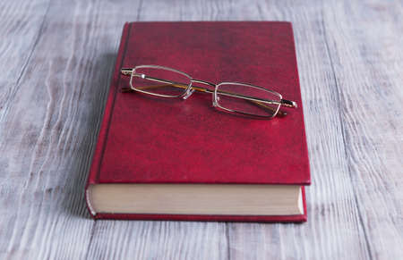 On a light background is a wooden red book in hard cover and glasses for poor vision to read