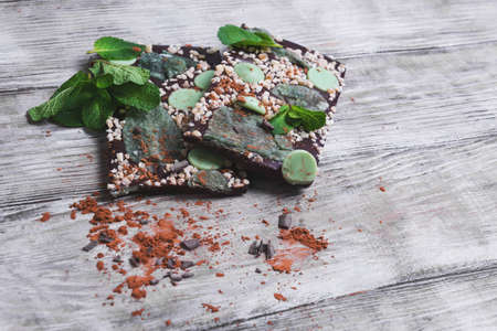 Chocolate, hand-made with mint leaves, candied violets, lemon candy, nuts, chips, cocoa powder on a light wooden background in rustic styleの写真素材
