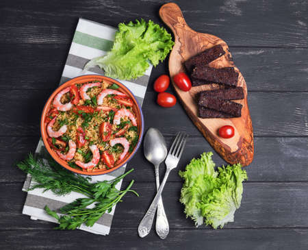 Blue ceramic bowl with couscous, parsley and dill, cherry tomatoes, bread croutons, cutting board olive wood, cloth, Distin fresh salad on a dark black wooden background, rustic, top viewの写真素材
