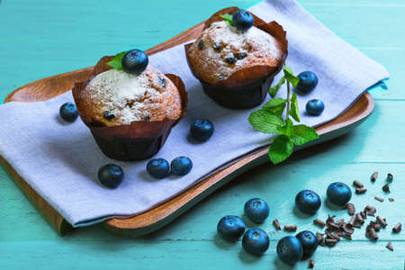 Muffins with berries blueberry cupcakes, sprigs of mint and grated chocolate shavings on a wooden tray on a green backgroundの写真素材