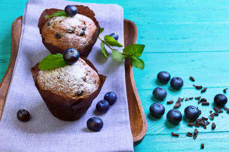 Muffins with berries blueberry cupcakes, sprigs of mint and grated chocolate shavings on a wooden tray on a green backgroundの写真素材