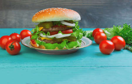 Sandwich on a round bun with sesame seeds cheeseburger cherry tomatoes on a green wooden backgroundの写真素材