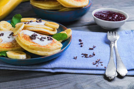 beautiful breakfast frieds banana fritter decorated additives, mint leaves, jam, grated chocolate, cloth towel on a gray wooden background in rustic styleの写真素材