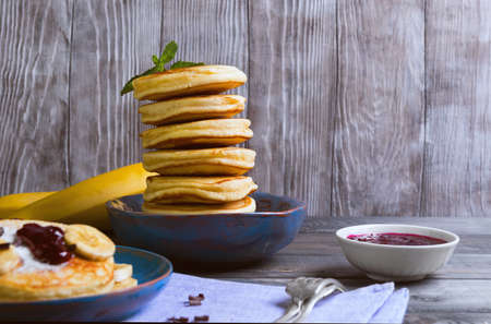 beautiful breakfast frieds banana fritters decorated additives, mint leaves, jam, grated chocolate, cloth towel on a gray wooden background in rustic styleの写真素材