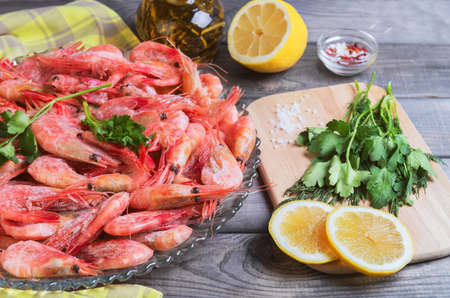 On a dark wooden table dish with shrimps raw, lemon oil in a glass bottle, dill, parsley, salt, pepperの写真素材