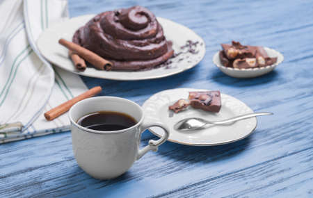 Round Twisted Bun Danish snail poured chocolate icing, white cup of coffee espresso, cinnamon sticks, pieces of chocolate with hazelnuts on a blue wooden backgroundの写真素材