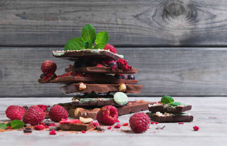 Tiles of a broken exquisite hand-made chocolate with dried and fresh berries, nuts, peel, mint, clean empty place for text, for the recipesの写真素材