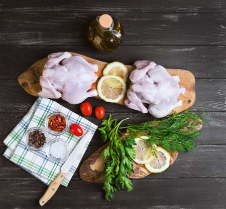 Two raw chicken carcasses, cherry tomatoes, dill, parsley, pepper, salt crystal, cutting board, bottle of olive oil on a wooden background in rustic style, top viewの写真素材