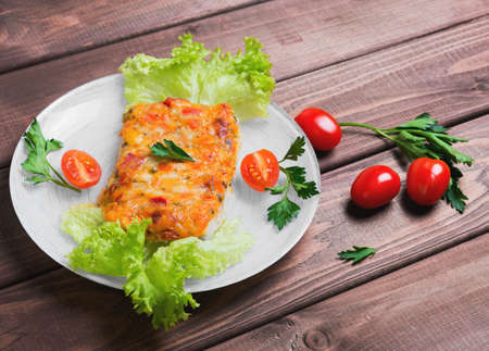 On a wooden table in a white plate glass portion of the baked cod fish with spices and herbs, cherry...