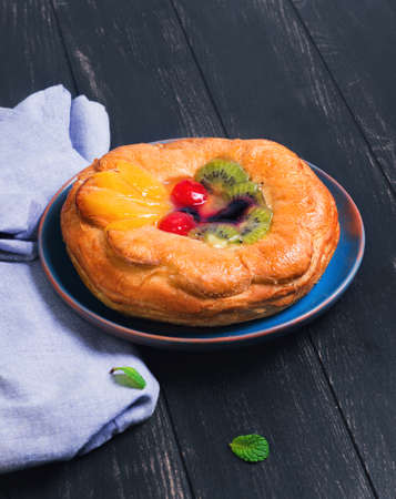 Denish fluffy bun with fruits and jelly on top, a glass of mojito, sliced lime, towel napkin, plate handmade ceramic on a dark wooden background in rustic styleの写真素材