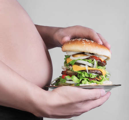 Man with a big fat belly cuddle and holding a plate with a high cheeseburgerの写真素材