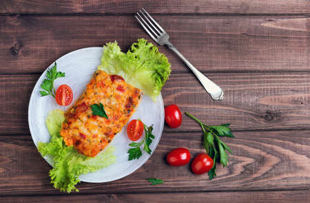 On a wooden table in a white plate glass portion of the baked cod fish with spices and herbs, cherry tomatoes, lettuce, parsleyの写真素材
