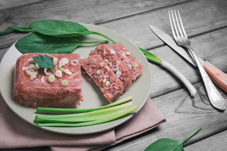 Jellied meat jelly on a green plate, young onions, spinach leaves on rustic vintage gray wooden backgroundの写真素材