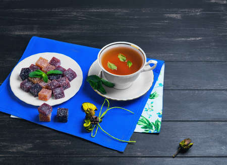 Berry-fruit marmalades cubes, tea and mint leaves on a dark black wooden background, empty place for...