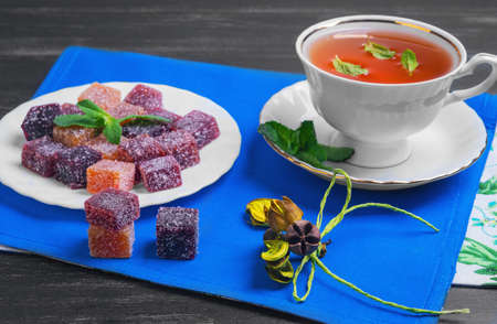 Berry-fruit marmalades cubes, tea and mint leaves on a dark black wooden backgroundの写真素材