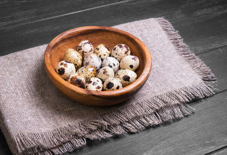 Quail eggs in a wooden bowl on sacking on a black wooden surfaceの写真素材