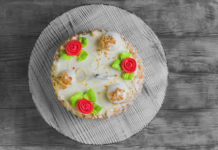 Cream biscuit cake with roses and meringue with nuts on a stand on a white background worn wooden surface with a single candle for birthday, top viewの写真素材