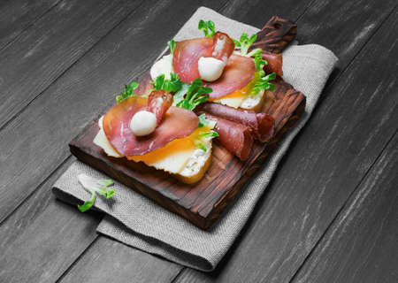 Two sandwiches bruschetta with jerked meat, ricotta cheese, mozzarella, lettuce on a sacking, wooden...