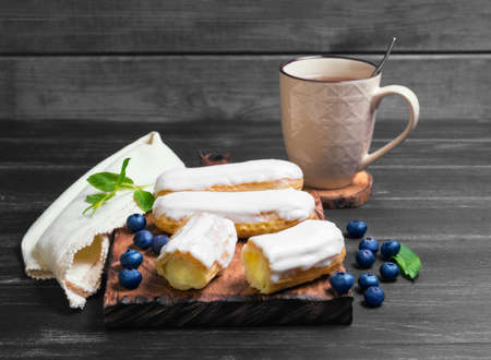 Morning breakfast Cakes French eclairs with white icing, mint, drink on a cutting board on a dark...