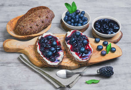 Sweet berry crostini sandwiches with blackberry jam and berries blueberries, whole grain bread for sandwiches, sandwiches board, spoon, mint leaves on a bright white background woodenの写真素材