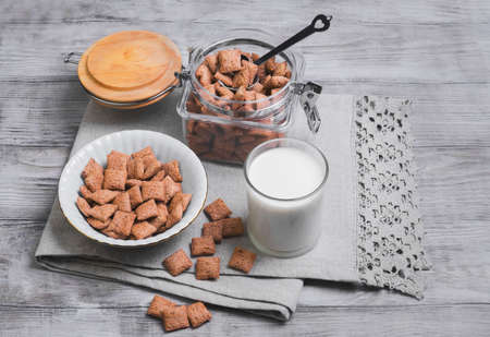 Multigrain healthy cereal corn pads chocolate in a white bowl for milk breakfast, glass of milk, cereal bank, cereal is scattered on a table on a light wooden background surfaceの写真素材