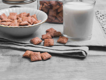 Multigrain healthy cereal corn pads chocolate in a white bowl for milk breakfast, glass of milk, cereal bank, cereal is scattered on a table on a light wooden background surfaceの写真素材