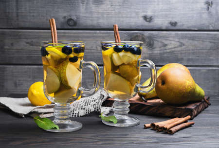 Two pears cocktails in glasses, ingredients for cocktails and fresh whole pears, lemons, blueberries, mint leaves, cinnamon sticks, burlap cloth, wooden board on a dark background in rustic styleの写真素材