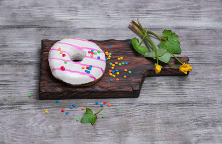 Donut with white and pink icing, sprinkled sprinkling colored for donuts, yellow flowers on a light wooden backgroundの写真素材