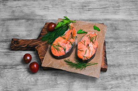 steaks salmon fish on a cutting board, parsley, dill on a light wooden background surfaceの写真素材