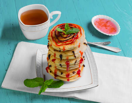A stack of fresh pancakes sprinkled with jam and top with chocolate, jam with rose petals, a cup of...