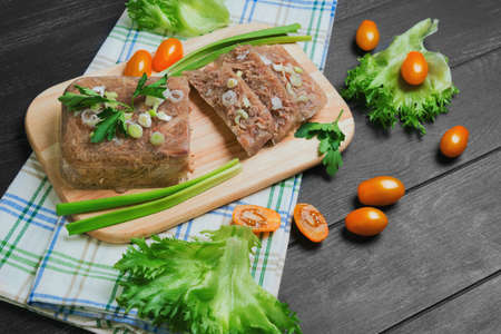 Meat jelly aspic galantine, yellow cherry tomatoes, parsley, lettuce, wooden cutting board, on a dark black background surfaceの写真素材
