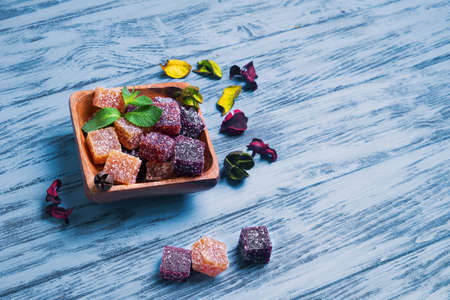 Berry marmalade jelly cubes in a wooden square Moscow on blue wooden background surface, a sprig of mint, dried flowers, empty place for text, recipeの写真素材