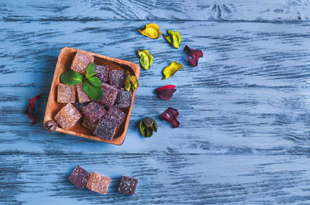Berry marmalade jelly cubes in a wooden square, pieces of marmalade on the table on blue wooden background surface, a sprig of mint, dried flowers, empty place for text, recipe, top viewの写真素材