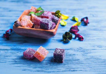 Berry marmalade jelly cubes in a wooden square, pieces of marmalade on the table on blue wooden background surface, a sprig of mint, dried flowersの写真素材
