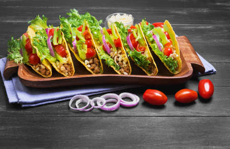 Mexican food tacos, peppers, cherry tomatoes, grated cheese, minced meat in a corn tortilla on a tray on a linen towel on a black wooden backgroundの写真素材