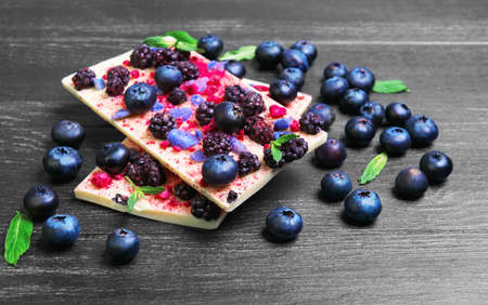 Handmade chocolate bars white, Ingredients for white chocolate blackberries, blueberries, blueberry, raspberry, candied violet petals, mint leaves, candy heart on a dark black background wooden surfaceの写真素材
