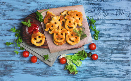 Food French fries potatoes for kids children smiling face, ketchup, parsley, lettuce, cherry pomidlory cloth napkin on cutting board on blue wooden background, top viewの写真素材