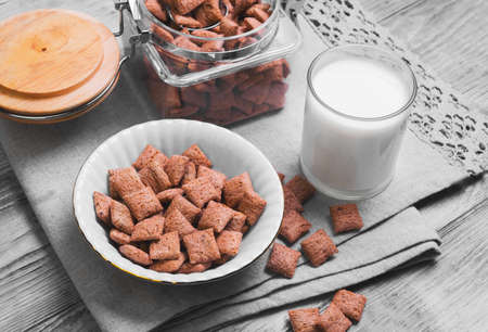 Multigrain healthy cereal corn pads chocolate in a white bowl for milk breakfast, glass of milk, cereal bank, cereal is scattered on a table on a light wooden background surfaceの写真素材