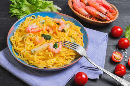 Tagliolini Pasta spaghetti with shrimps and vegetables courgettes zucchini, cherry tomatoes, fresh lettuce, shrimps in a bowl on a dark black wooden backgroundの写真素材