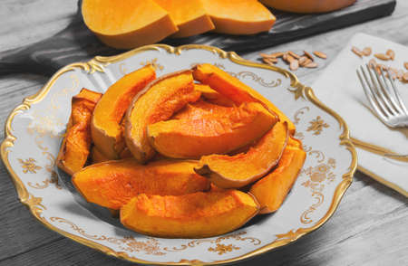 Baked pumpkin pieces on white vintage porcelain plate, raw pumpkin pieces cut for baked, napkin tissue, pumpkin seeds on a bright white background woodenの写真素材