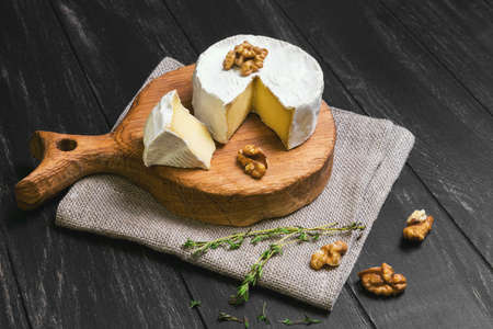 Camembert cheese and cut a slice, walnuts, thyme, sacking on a cutting board on a dark black wooden backgroundの写真素材